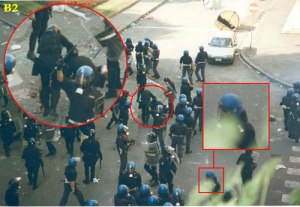 Piazza Alimonda, Genova, h. 17:30 circa del 20 luglio 2001. I tutori dell'ordine hanno appena massacrato di botte il fotografo Eligio Paoni, colpevole di aver fotografato da vicino - e troppo presto - il corpo di Carlo Giuliani, e hanno metodicamente distrutto la sua Leica. Nel cerchio rosso, un agente lo trascina sul corpo e gli preme la faccia su quella insanguinata di Carlo (ancora vivo). Non è difficile immaginare cosa gli stia dicendo. Cosa non si doveva sapere delle condizioni del ragazzo in quel momento? Forse la risposta riguarda un sasso, un sasso bianco come il latte che si muove da un punto all'altro del selciato, scompare e ricompare, e a un certo punto è imbrattato di sangue.